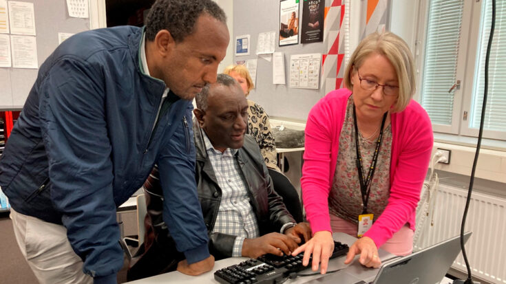 Nainen ja kaksi miestä tietokonetta tutkimassa.